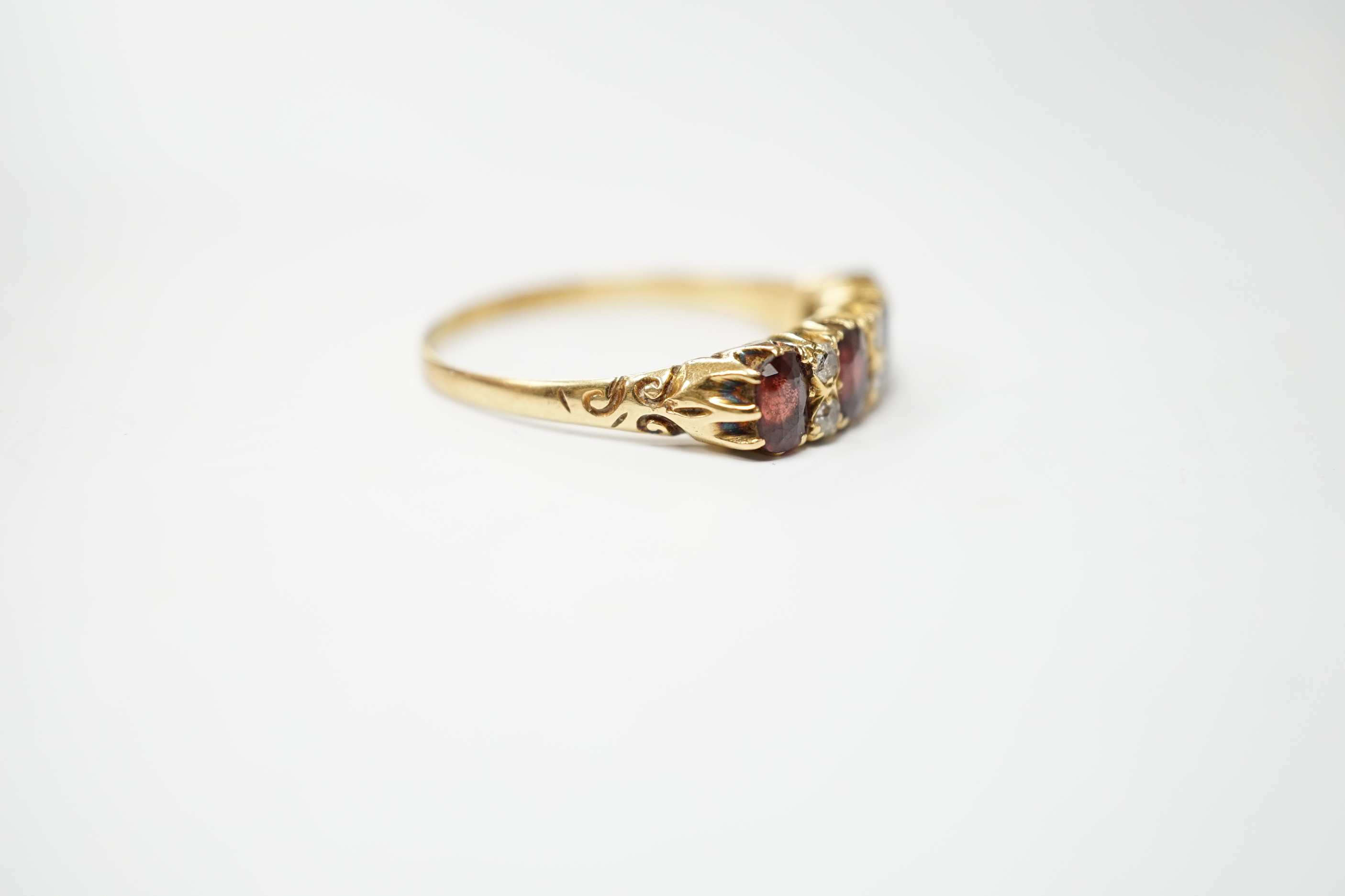 An Edwardian 18ct gold and four stone garnet set half hoop ring, with diamond chip spacers, size R, gross weight 3.6 grams.